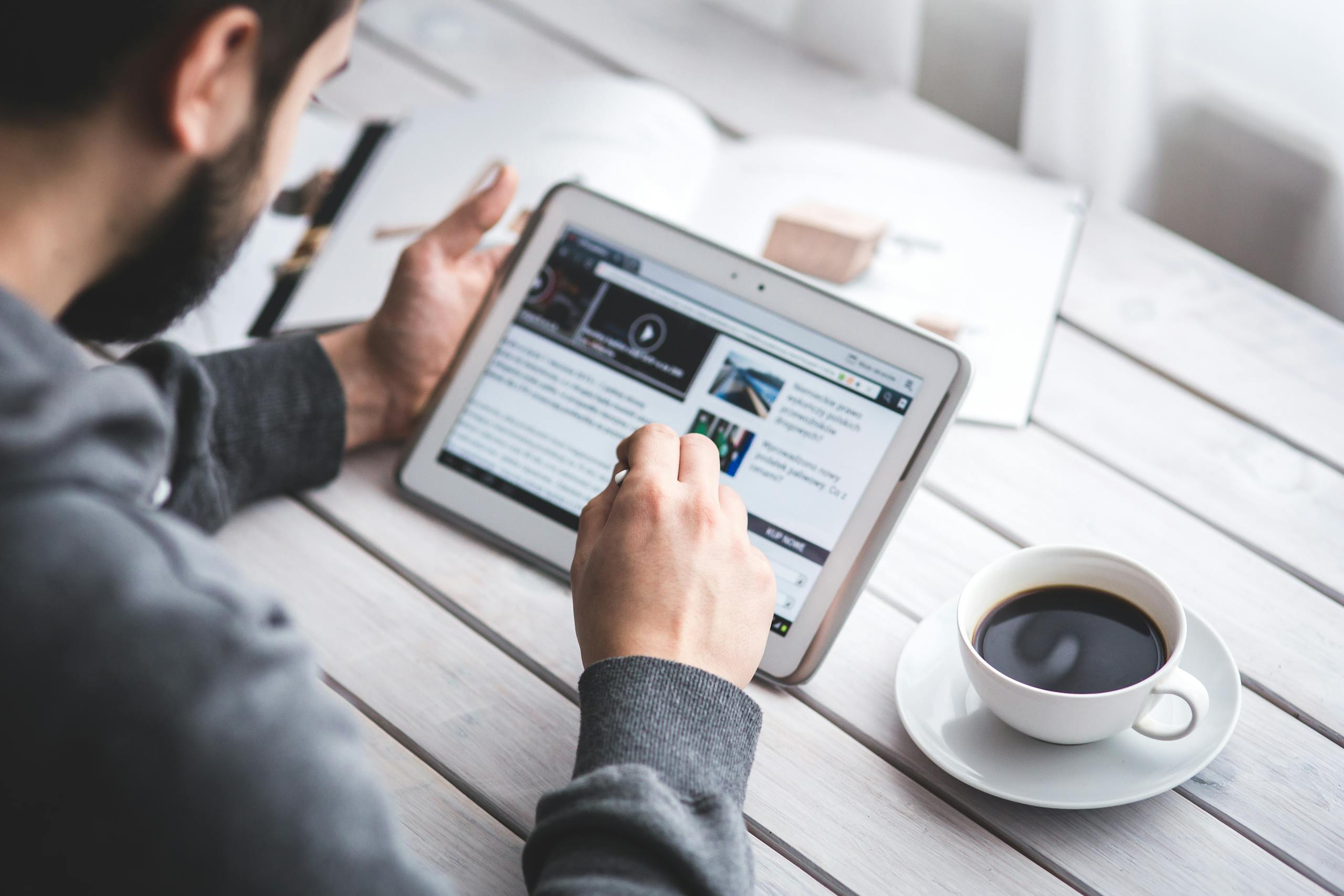 Course Selection for Study Abroad 1 A man uses a tablet to browse news while enjoying a cup of coffee, stylus in hand.